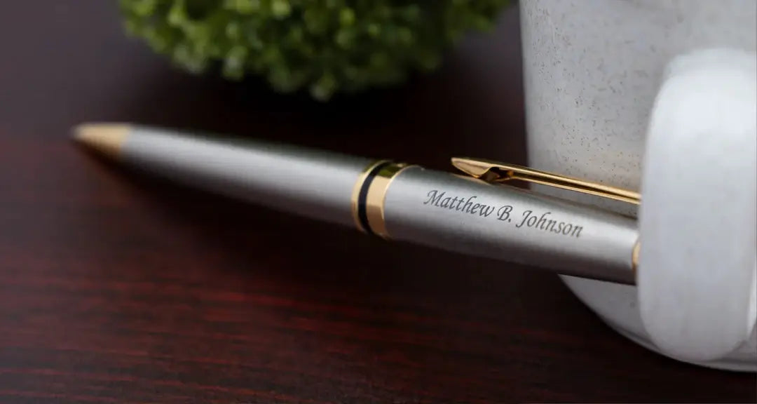 Engraved Expert Ballpoint Stainless Gold Trim next to teacup