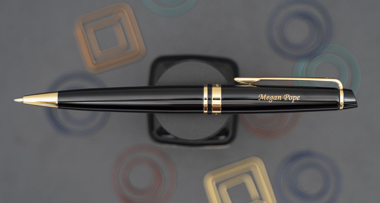 A black Waterman expert ballpoint resting on top of a bottle with an engraving on the cap.