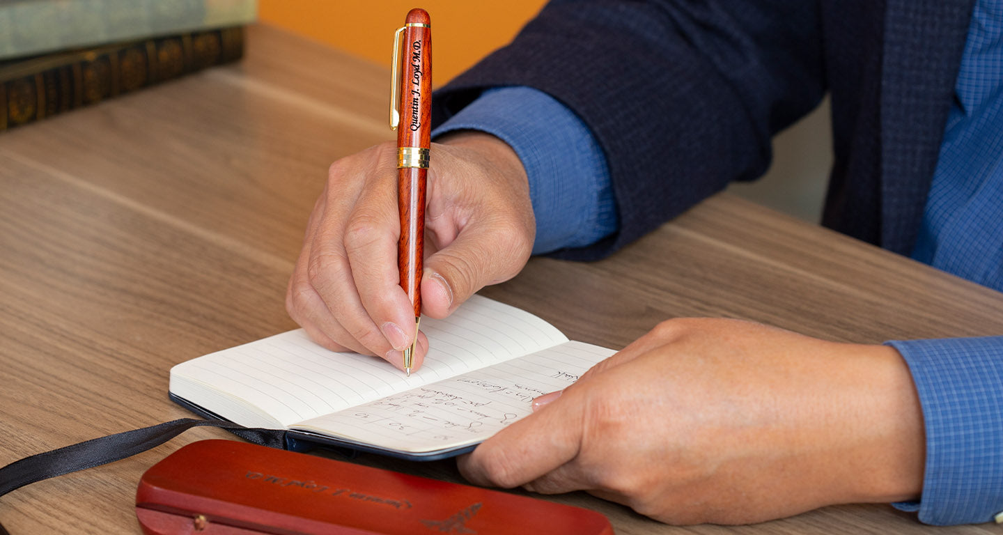 A man writing in a notebook with a wood pen with wood gift box lying on desk