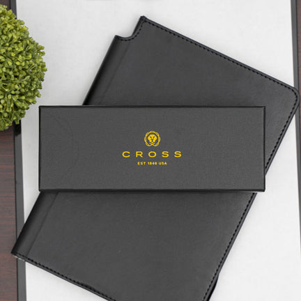 A gift box with cross pens logo on the top lying on a black notebook.