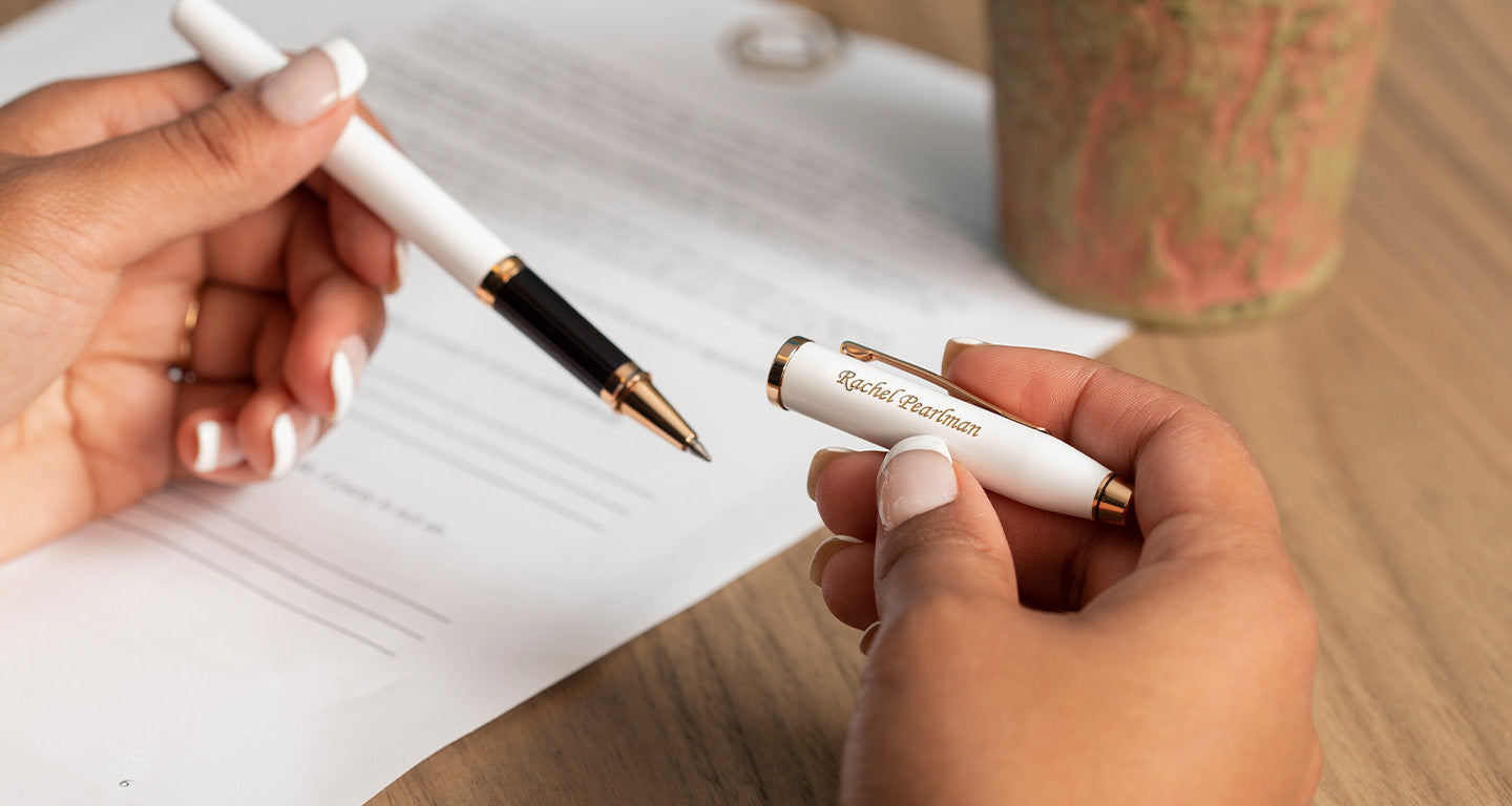 A white Cross Century II pen held by a woman with her hands resting on the desk.