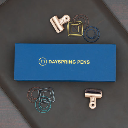 A gift box with a Dayspring Pens logo on it lying on a leather padfolio