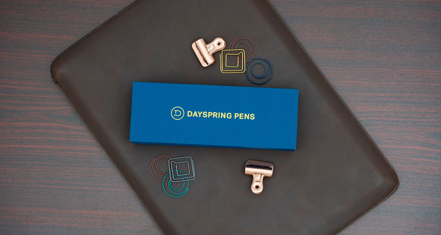 Dayspring Pens Box on top of leather folder with paper clips around it