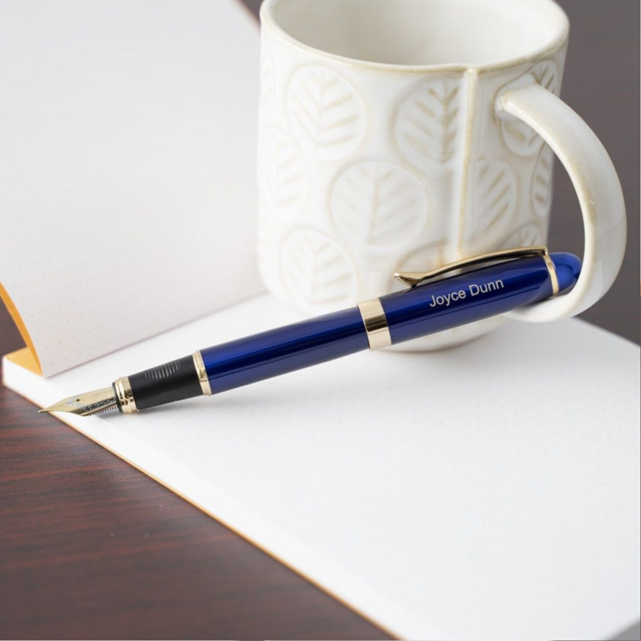 Engraved Alexandria Blue Fountain Pen on top of notebook next to coffee mug