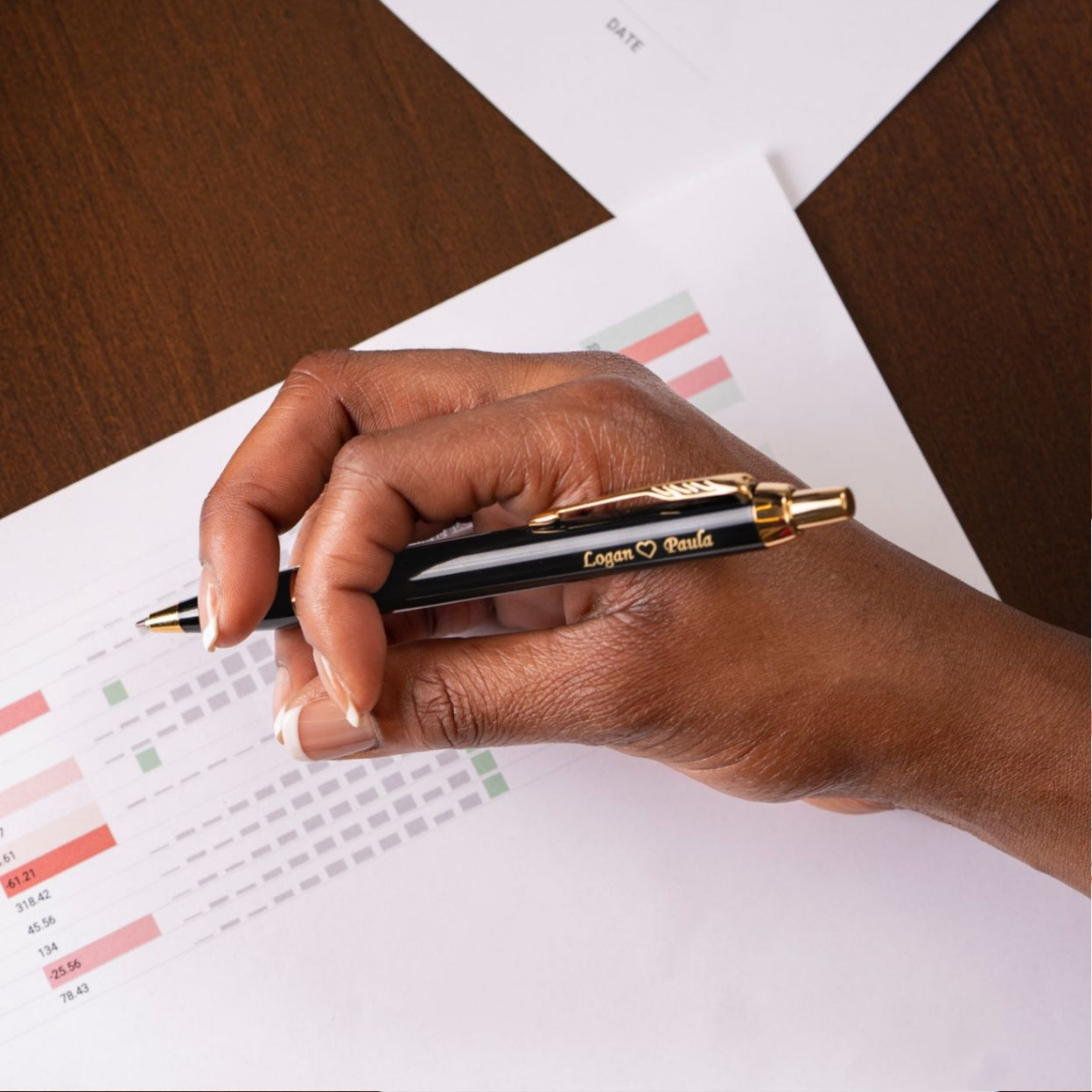 Woman holding engraved IM Gold and Black Ballpoint with spreadsheet
