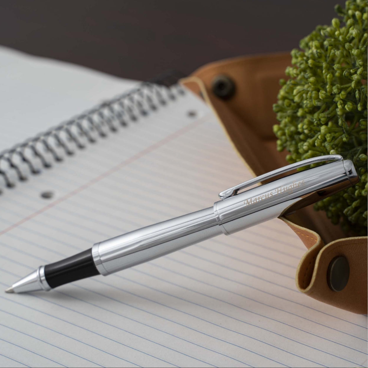 Engraved Abingdon Chrome Rollerball on top of notebook next to plant