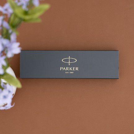 A Parker pens gift box lying on a brown surface with flowers beside it