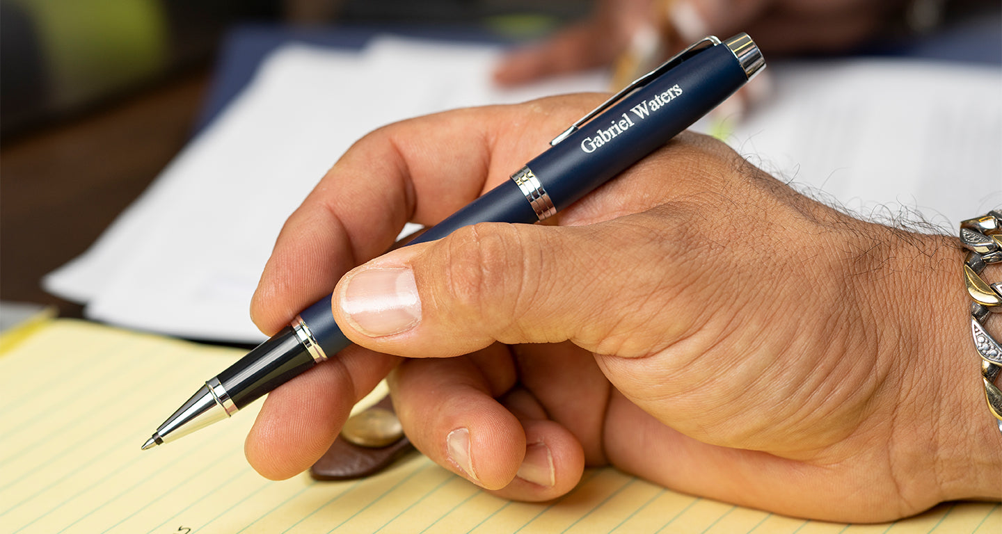 A blue Parker IM rollerball pen held by a man over a notepad.
