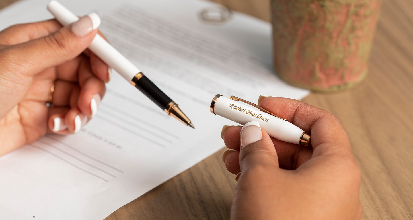 White Cross Century II Rollerball pen being uncapped by a woman with hands on a desk.