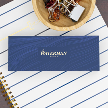 A Waterman Pens gift box lying on a white notebook.
